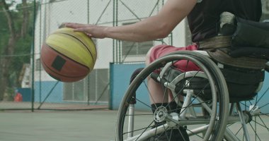 Belden aşağısı felçli bir erkek sporcu dışarıda meslektaşından top alıyor. Dışarıda spor salonunda basketbol oynayan iki engelli sporcu. Spor ve sakatlık kavramı