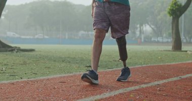 Orta yaşlı engelli bir atletin ön görüntüsü protez bacaklı bir sporcunun koşan pistte kameraya doğru yürümesi.