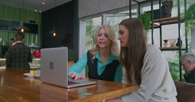 Üst düzey bir kadın yönetici, kahve dükkanında dizüstü bilgisayarın önünde oturan genç bir kadına işi açıklıyor. Yaşlı kadın lider bilgisayar ekranını işaret ederek çalışanla iş hakkında konuşuyor. Protokolü tartışan iki kişi