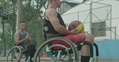 İki belden aşağısı felçli sporcu dışarıda basketbol oynuyor ve takım arkadaşına pas veriyor. Özürlü olarak azim ve spor