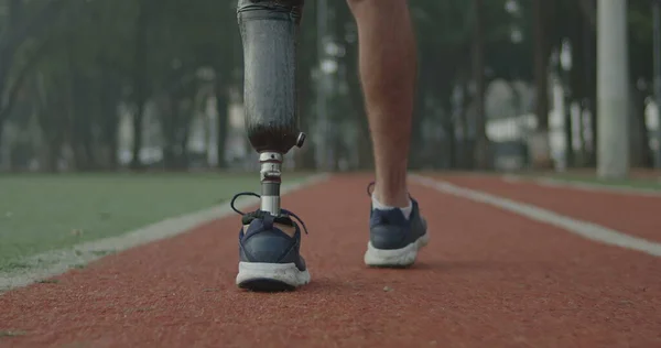 Back view of a disabled athlete man with prosthetic leg walking on running track