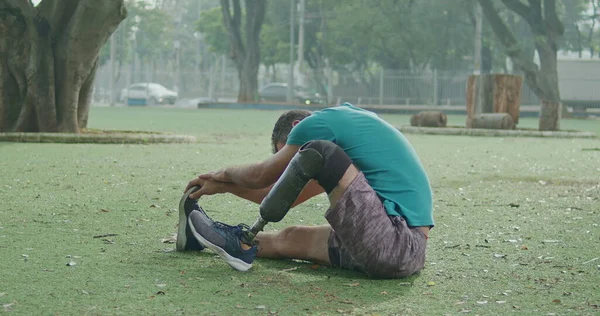 A middle aged disabled athlete man with prosthetic leg stretching body outdoors sitting