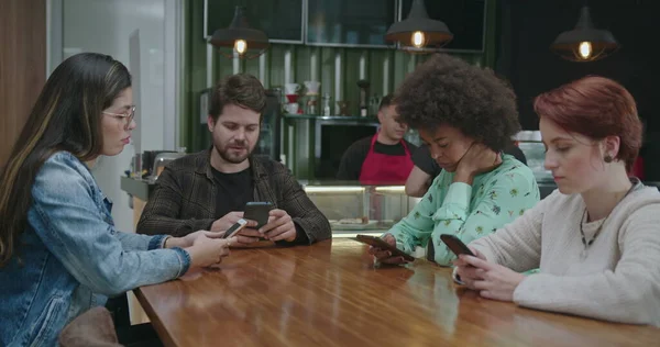Group of diverse people in front of their modern devices at coffee shop isolated together. Friends each in technological bubbles staring at smartphone screens