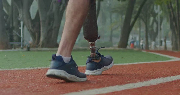 Side view of a disabled athlete man with prosthetic leg walking on running track