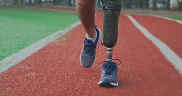 Front view of a disabled athlete man with prosthetic leg walking on running track
