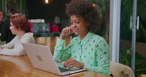 One happy black woman in front of laptop computer seated at coffee shop restaurant. An African American female worker looking at modern technology screen