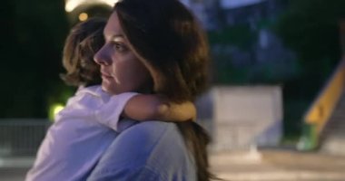 Anne, gece sokakta yürürken çocuğu kollarında tutuyor. Annem akşamları çocuğu taşıyor.
