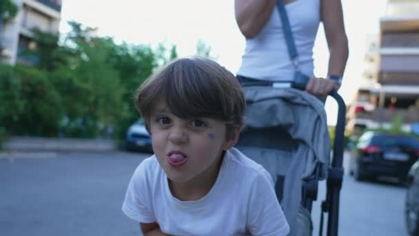 傻傻的小男孩坐在推车上伸出舌头 淘气的孩子做鬼脸 — 图库视频影像
