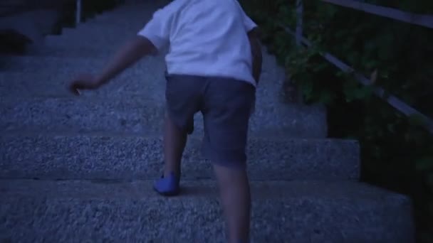 一个活泼的小男孩晚上爬上城市的楼梯 儿童练习特写腿爬楼梯 — 图库视频影像