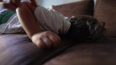 Ebeveyn çocuğu öğle uykusundan uyandırmaya çalışıyor. Küçük bir çocuk kanepede uyuyan çocuğu dürtüyor. Uyanma zamanı.