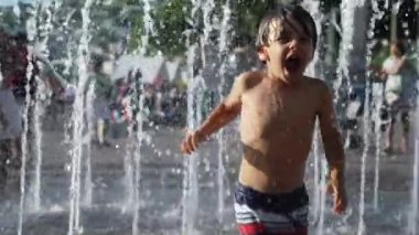 Mutlu çocuk sıcak yaz gününde 120 fps yavaş çekimde su parkı jetlerinde eğleniyor.