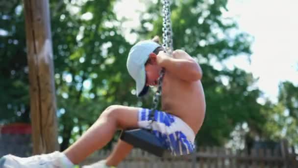 夏の日の間に遊び場のスイングで回転する小さな男の子 子供のスピンは楽しい — ストック動画