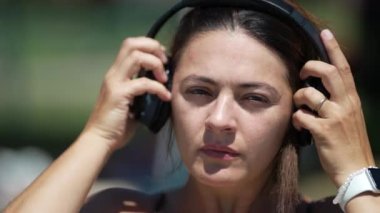 30 'lu yaşlarda bir kadın, kulaklıkları çıkarırken gürültü yapıyor. Park 'ta kulaklık takan bir kadın.