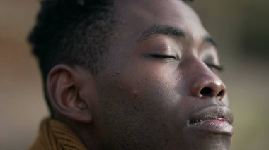 Düşünceli genç siyah adam meditasyonda gözlerini kapatıyor.