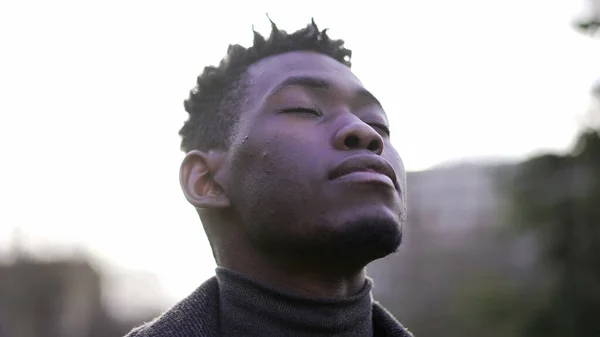 Contemplative black man looking at sky with HOPE and FAITH, closing and opening eyes
