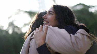 Two female friends hugging each other at park. Happy Women embrace reunion outdoors