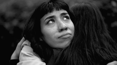 A depressed latin woman having the support of friend. Two women hugging each other in monochromatic. Sad person closeup face