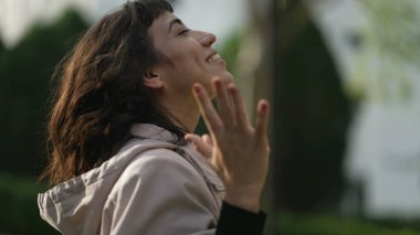 Evangelical South American woman standing outside feeling the presence of God arms in the air looking at sky with FAITH