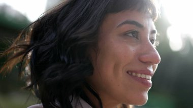 Happy woman standing in nature taking a deep breath closing eyes in contemplation. Meditative hispanic latina girl opening eyes to sky