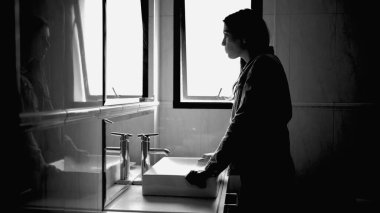 Suffering woman in front of bathroom mirror in mental disorder feeling anxiety in monochromatic