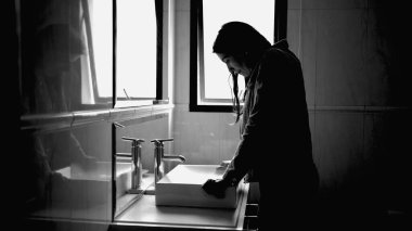 Suffering woman in front of bathroom mirror in mental disorder feeling anxiety in monochromatic