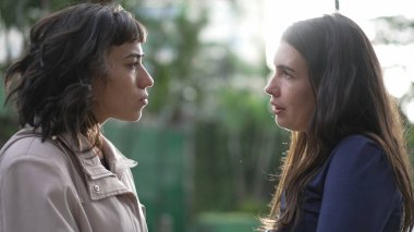 Two women in conversation standing outside at park. Female friends talking to each other