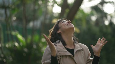 Evangelical South American woman standing outside feeling the presence of God arms in the air looking at sky with FAITH