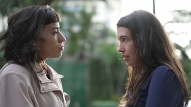 Two women in conversation standing outside at park. Female friends talking to each other