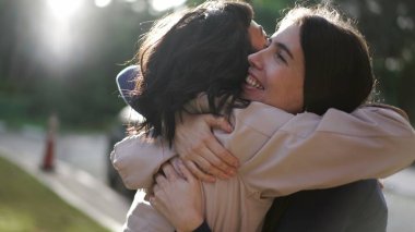 Two happy female best friends hugging each other. Women embrace reunion outdoors at park