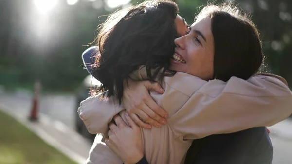 Two happy female best friends hugging each other. Women embrace reunion outdoors at park