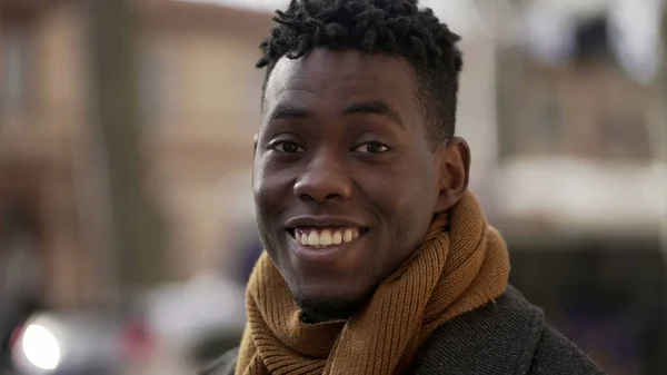 Friendly black african man portrait smiling at camera standing outdoors in urban city wearing scar furing cold season