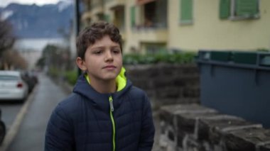 Düşünceli genç bir çocuk şehir caddesinde yürüyor. Ergen erkek çocuk şehir kaldırımında yürüyor. Kışlık ceket giyen düşünceli bir insan.
