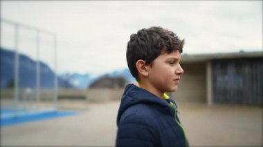 Şehir parkının dışında ciddi bir ifadeyle duran düşünceli genç bir çocuk. Düşünceli, yakışıklı, çocukluk çağında erkek çocuk, tefekkür için kışlık kıyafetler giyiyor..
