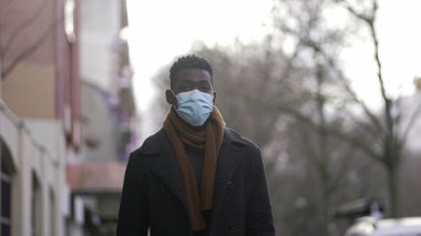 Black man wearing covid face mask walking outside in city downtown