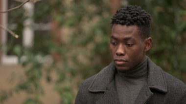 Düşünceli siyah Afrikalı adam dışarıda durup düşünüyor, dalgın dalgın gökyüzüne bakıyor.
