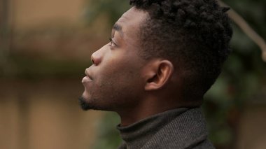 Pensive black African man standing outdoors thinking, looking up at sky in contemplation