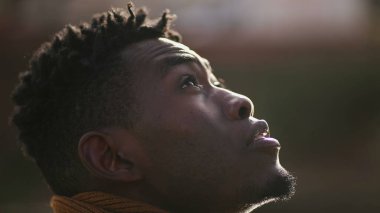 Pensive black African man standing outdoors contemplating life and spiritual path looking up at sky