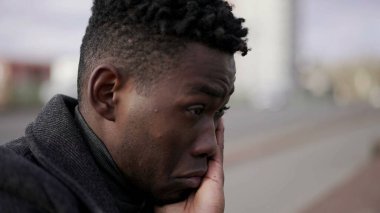 Düşünceli siyah Afrikalı adam şehrin kaldırımında oturuyor ve duygusal acı çekiyor.