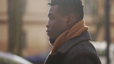 Düşünceli siyahi bir adam kış mevsiminde şehirde tek başına dolaşarak çekim yapıyor.