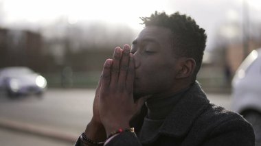 Preoccupied black African man sitting at city street curb feeling anxiety