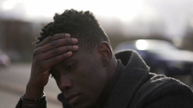 Kafası meşgul siyah Afrikalı adam şehir kaldırımında oturuyor. Endişe duyuyor.