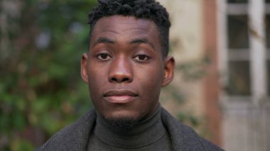 Genç siyahi adamın dışarıda durup kameraya baktığı portre.