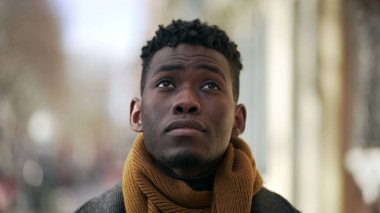 Düşünceli, düşünceli, siyahi Afrikalı adam dışarıda durup şehri izliyor.