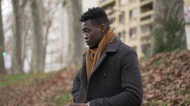 Pensive thoughtful African black man standing outside at park thinking about life