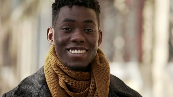 Portrait black African male smiling at camera wearing scarf outside in city