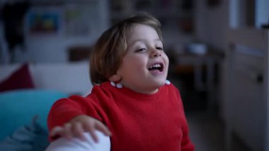 Mutlu, küçük bir çocuğun portresi. Kapalı bir evde, oturma odasında dikiliyor. 2 yaşında kırmızı kazak giyen bir çocuk.