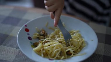 Çocuk tek başına spagetti yiyor. Küçük bir çocuk çatalla erişte yiyor.