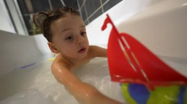 Küçük bir çocuk oyuncak tekneyle küvette oynuyor. Küvette banyo yapan neşeli çocuk.