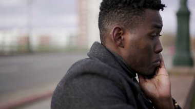 Kafası meşgul siyah Afrikalı adam şehir kaldırımında oturuyor. Endişe duyuyor.