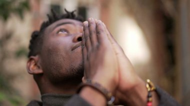 Dindar genç siyahi adam Tanrı 'ya dua ediyor. Afrikalı insan gökyüzüne umutla ve FAITH2 ile bakıyor
